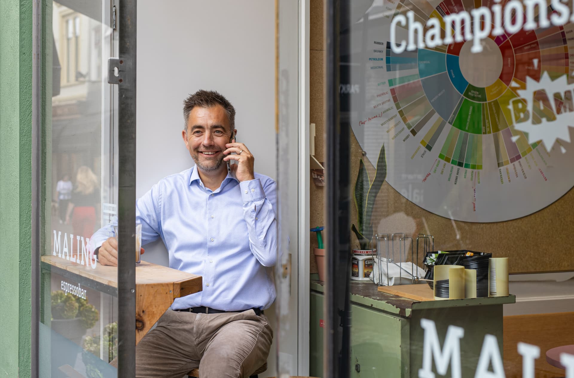 Siemon van Dam lachend aan de telefoon in de deuropening van een espressobar